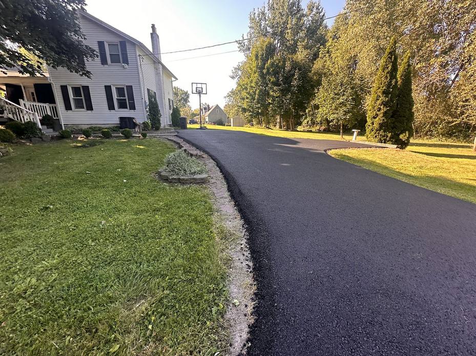 Newly replaced asphalt driveway running alongside a white house