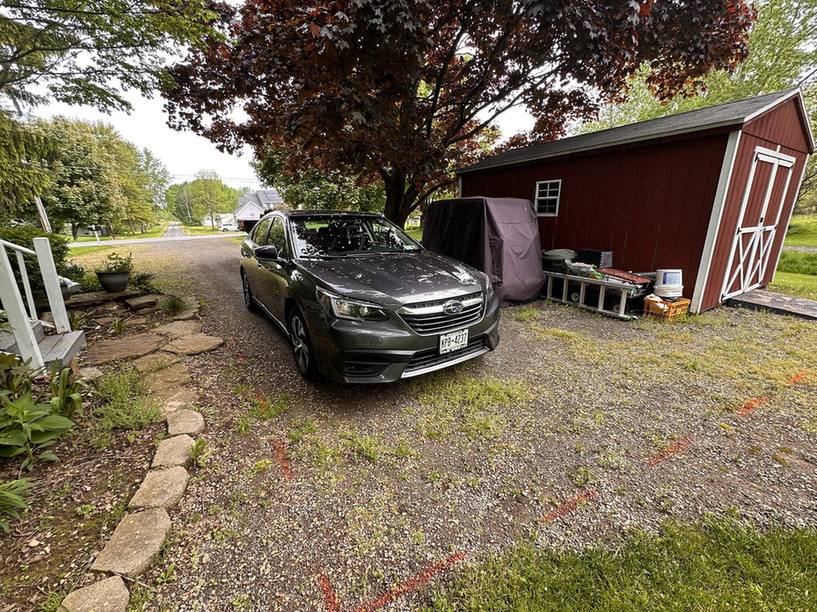 Gravel driveway with a parked car beside a red shed before paving