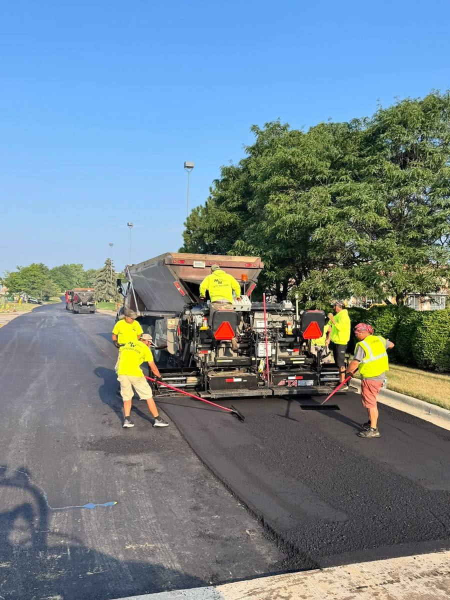Paving crew raking hot asphalt behind a paver as a truck feeds it mix