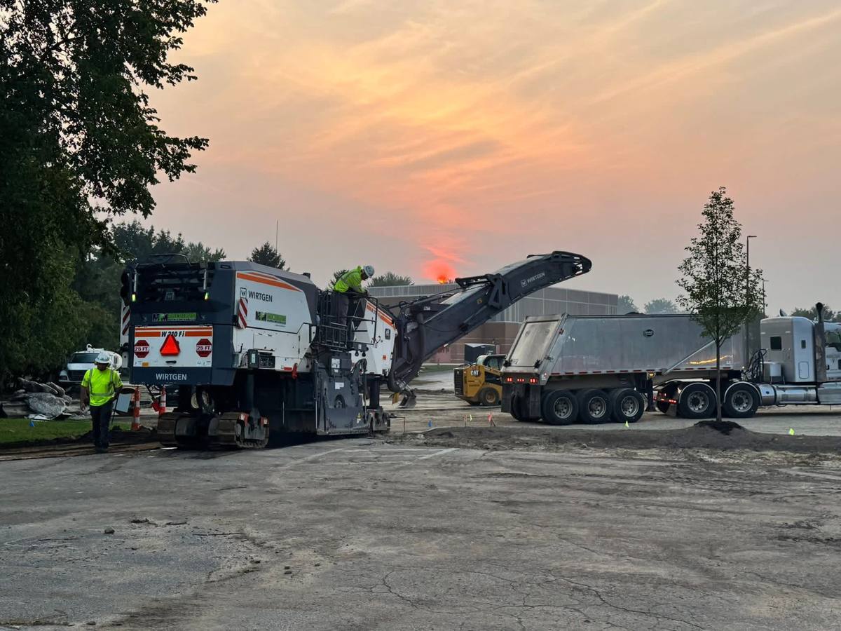 Milling machine grinding off old asphalt and loading it into a dump trailer at sunrise