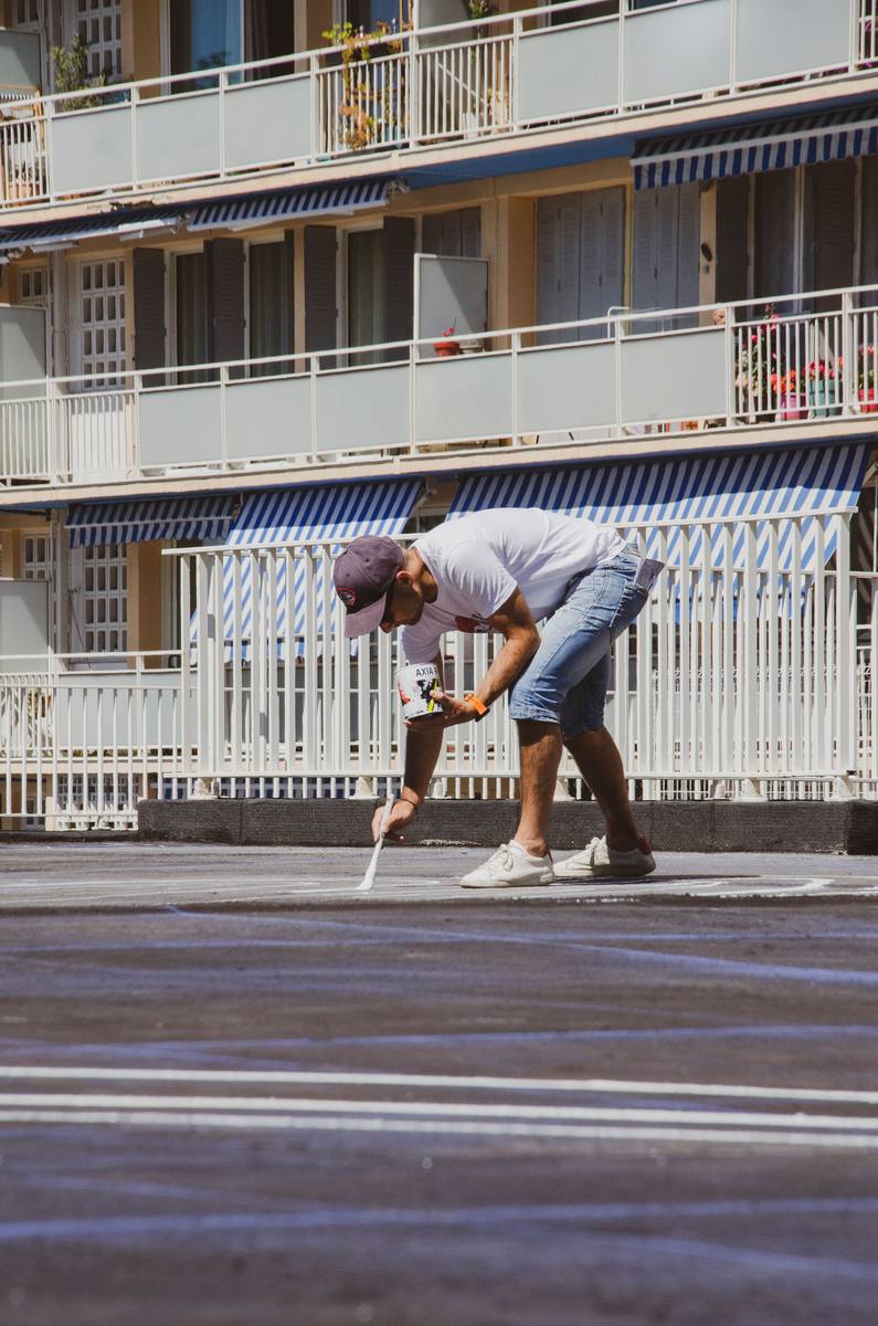 Worker painting a white line on parking lot pavement