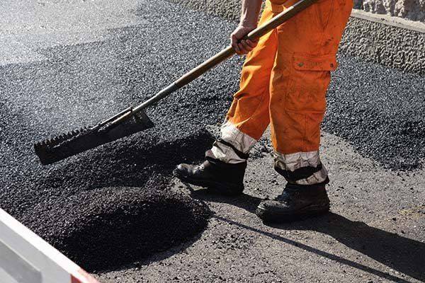 Worker raking hot asphalt into place