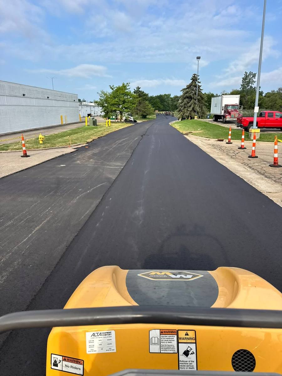 View from a roller seat over freshly paved asphalt beside a commercial building