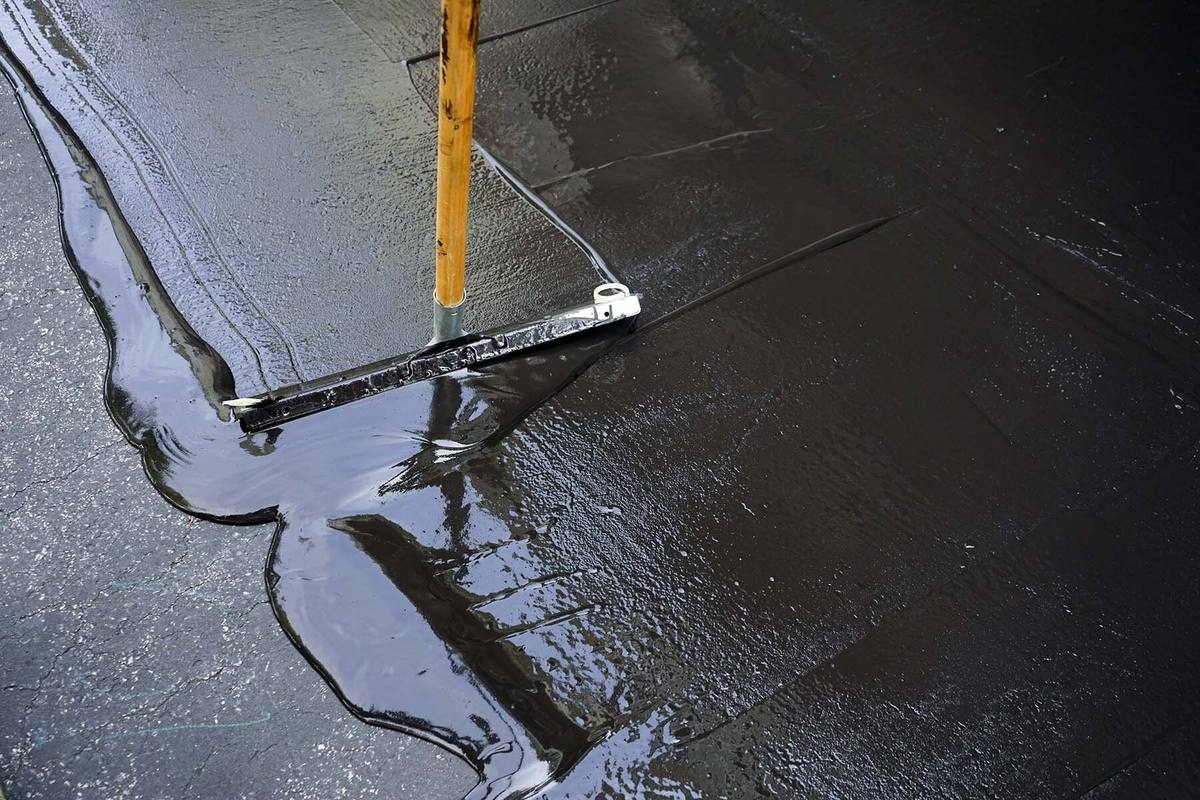 Close-up of fresh black sealer being spread across asphalt with a squeegee