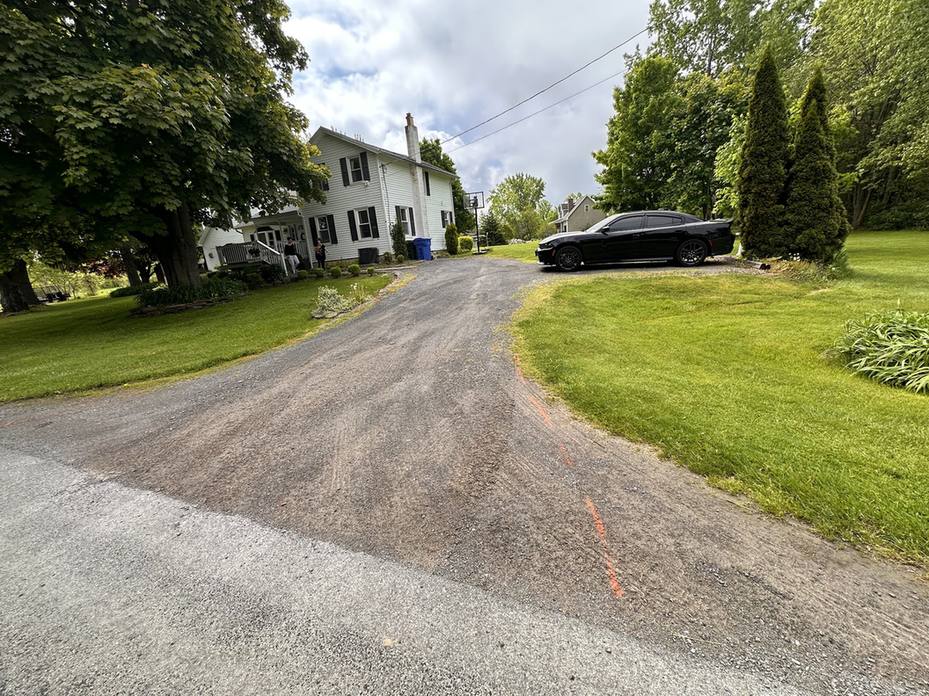 Worn gravel and broken surface driveway leading to a house